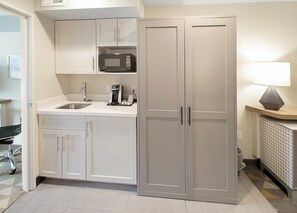 Une cuisine moderne avec des meubles blancs, un four à micro-ondes encastré, une machine à café et un évier.