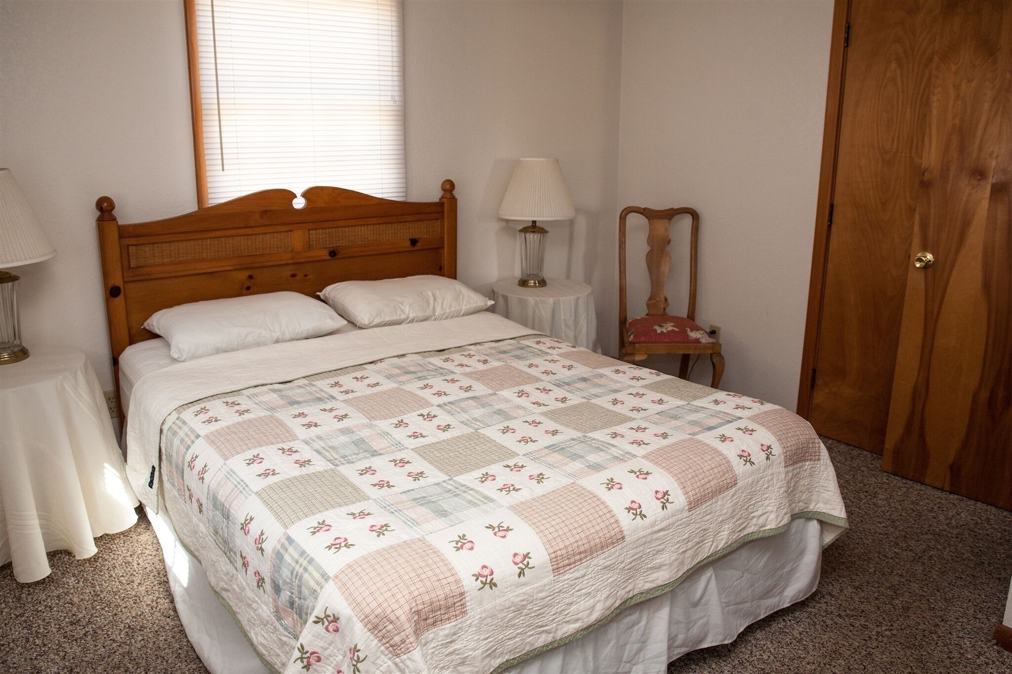 Een slaapkamer met een houten bed, een nachtkastje met een lamp, een spiegel en een deur.