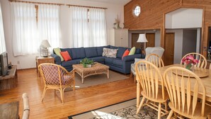 A cozy living room with a blue sofa, wooden dining table, wicker chairs, and a wooden ceiling. - Chez-toni 3 Bedroom Cottage by RedAwning (Avon)