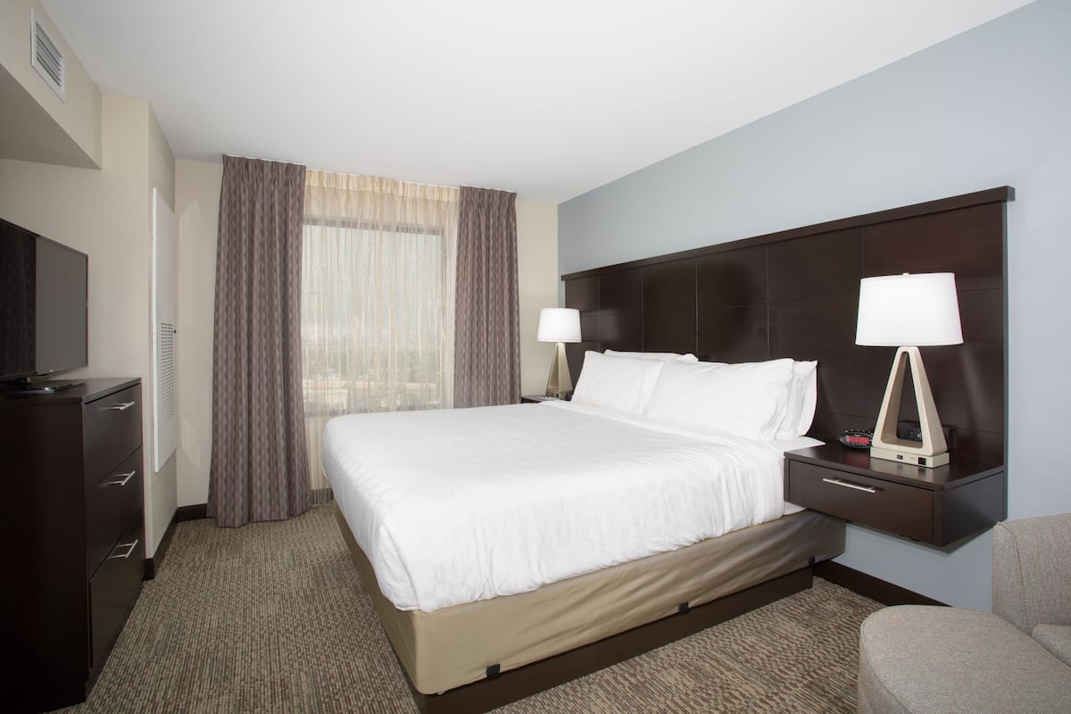 A hotel room with a large bed, bedside tables with lamps, a TV, and a window with curtains.