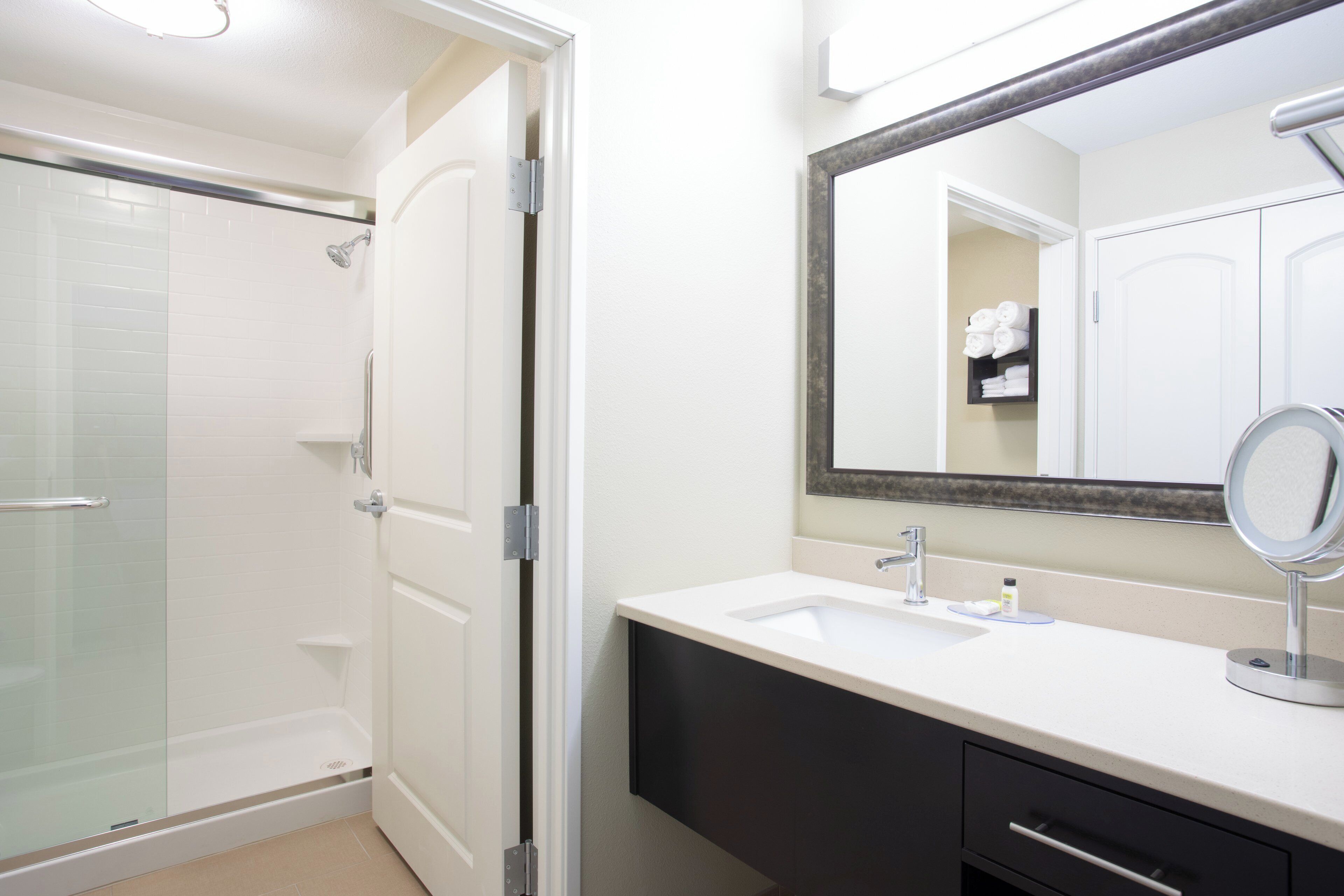 A bathroom with a glass shower enclosure, a white sink with a mirror, and a dark vanity.