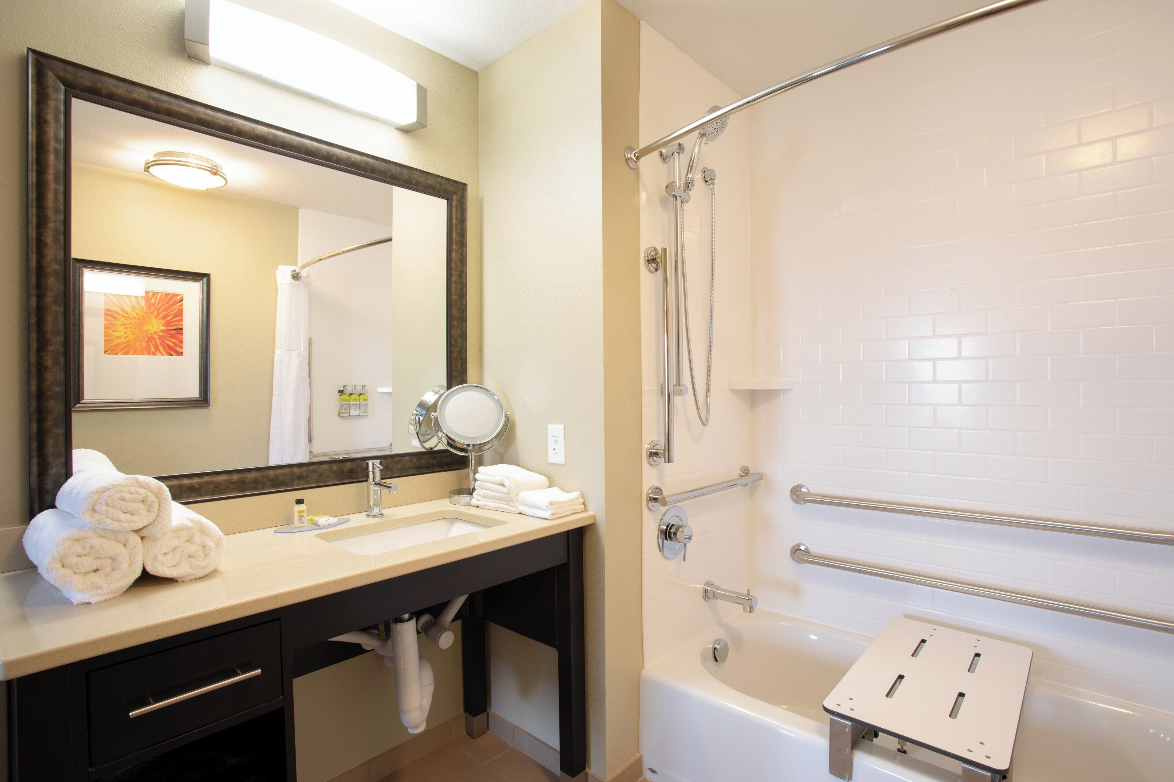 A hotel bathroom with a sink, mirror, towel rack, and a shower area.