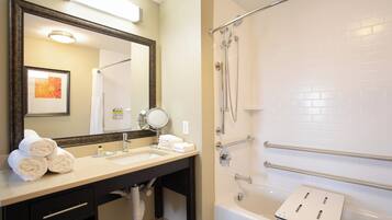 A hotel bathroom with a sink, mirror, towel rack, and a shower area.