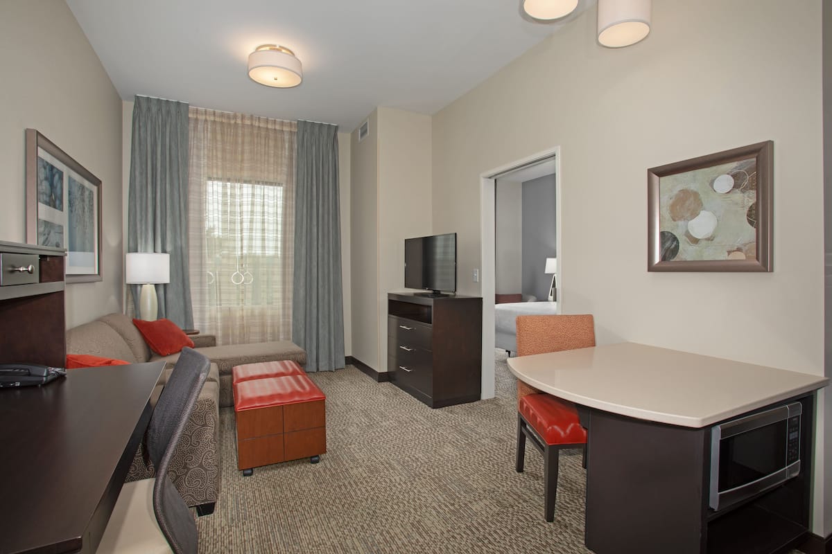 A hotel room with a sofa, a small table, a TV, a microwave, and a painting on the wall.