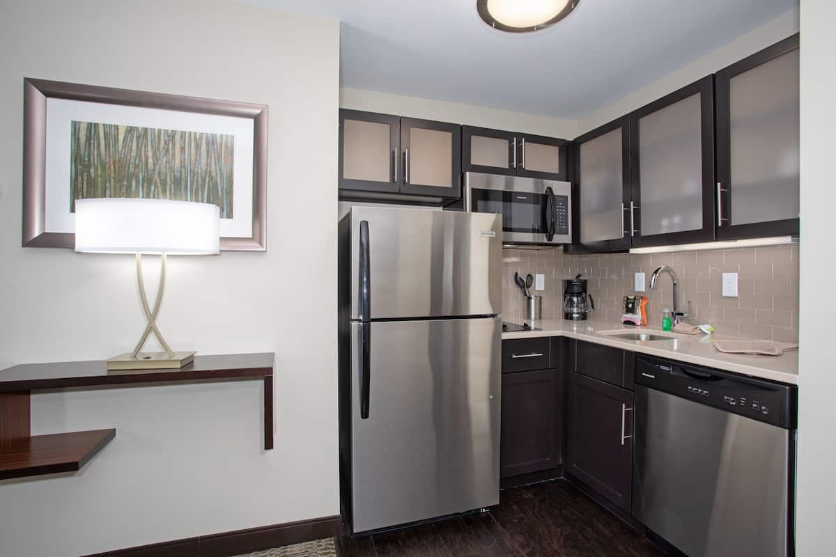 A modern kitchen with stainless steel appliances, dark cabinetry, and a countertop with a coffee maker and other items.