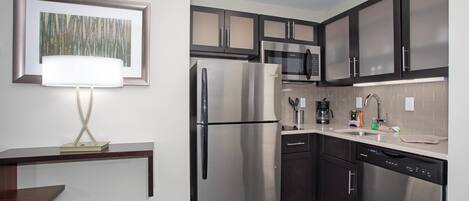 A modern kitchen with stainless steel appliances, dark cabinets, and a countertop with a coffee maker and utensils.