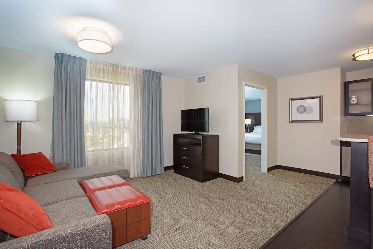 A hotel room with a sofa, a TV, a small cabinet, and a bathroom visible through an open door.