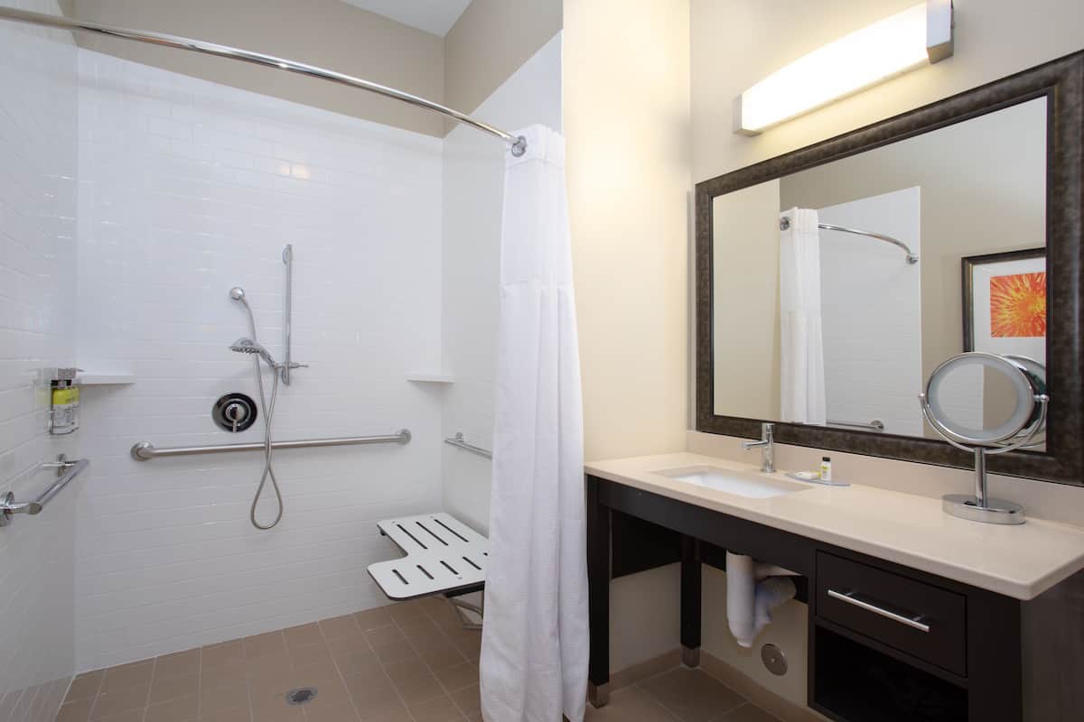 A bathroom with a shower, a sink, a mirror, and a towel rack.