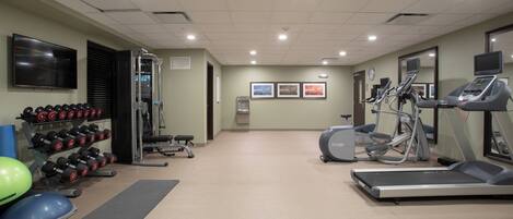 A gym with exercise equipment, a television, and a water dispenser.