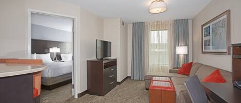A hotel room with a bed, a desk, a TV, a sofa, and a window with curtains.