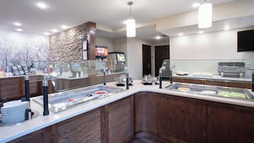 Zona de buffet con diversas opciones de comida, un refrigerador de Coca-Cola y una vitrina de vidrio.