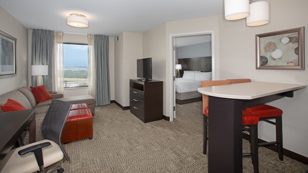 Habitación de hotel con sofá, escritorio con silla, televisión, cama y ventana con cortinas.