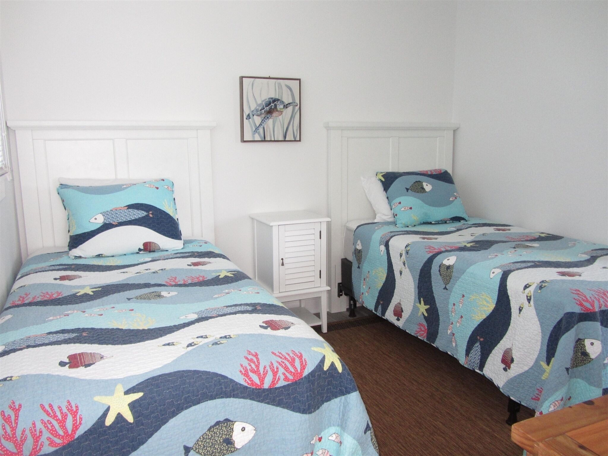 Quarto com duas camas, cada uma com colcha azul e branca com tema náutico.