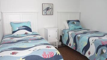 Quarto com duas camas, cada uma com colcha azul e branca com tema náutico.