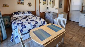 Un dormitorio con cama, escritorio, silla, ventilador de techo, televisor y un reloj en la pared.