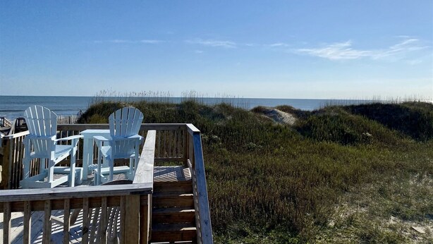A wooden deck with white chairs and a table overlooking a beach with dunes and the ocean. - 11 Mystical Sundaze Studio Bedroom Condo by RedAwning (Hatteras)
