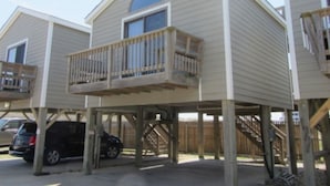 A row of beach houses with wooden balconies, a car parked in front, and a wooden fence in the background. - 11 Mystical Sundaze Studio Bedroom Condo by RedAwning (Hatteras)
