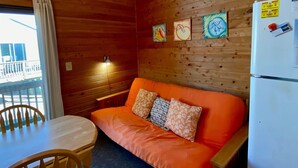 A cozy cabin room with a wooden interior, a sofa with patterned cushions, a dining table with chairs, and a refrigerator with magnets. - 11 Mystical Sundaze Studio Bedroom Condo by RedAwning (Hatteras)