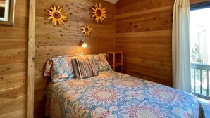 A wooden room with a bed, patterned bedding, and decorative sun motifs on the wall. - 11 Mystical Sundaze Studio Bedroom Condo by RedAwning (Hatteras)