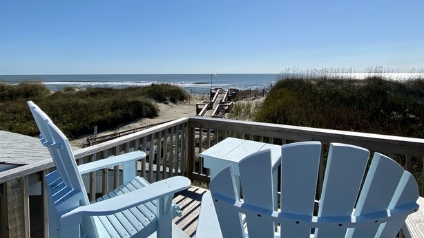 A wooden deck with two Adirondack chairs overlooking a beach with a fence and grassy dunes. - 12 Beach Fantasy Studio Bedroom Condo by RedAwning (Hatteras)