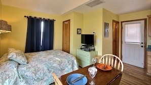 A room with a bed, a table with a plate and cutlery, a television on a dresser, and a door with a window. - 12 Beach Fantasy Studio Bedroom Condo by RedAwning (Hatteras)