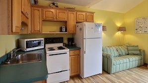 A compact kitchen with wooden cabinets, a microwave, a stove, and a refrigerator. - 12 Beach Fantasy Studio Bedroom Condo by RedAwning (Hatteras)