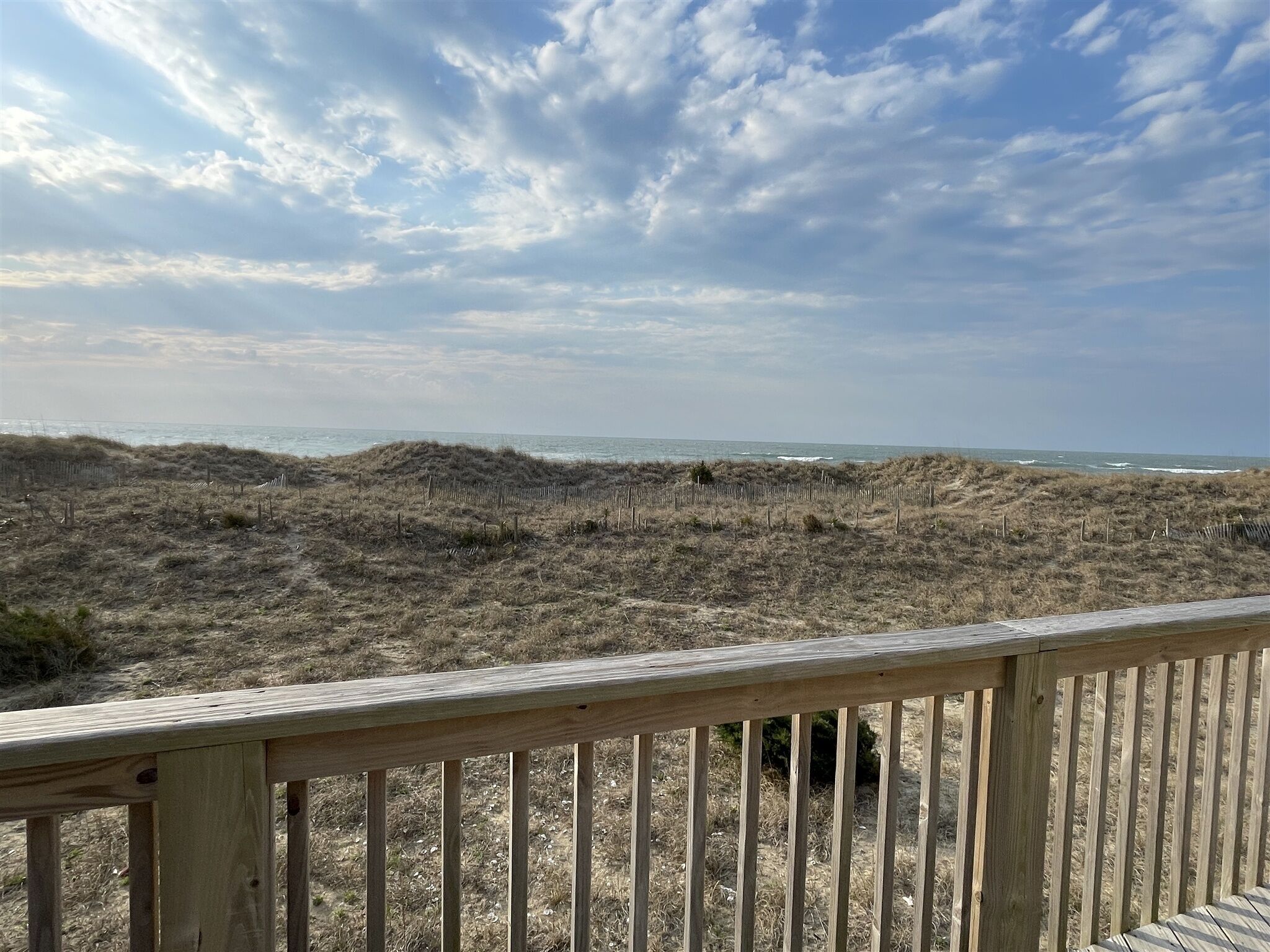 A beach view with a wooden deck and dunes in the background.