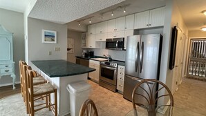 A modern kitchen with white cabinets, stainless steel appliances, a granite countertop, and a dining area with wooden chairs.