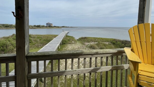 A wooden deck with a view of a calm body of water and a distant house.