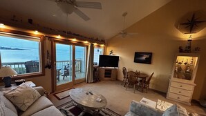 A living room with a sofa, chairs, a coffee table, a TV, and a balcony with a view of the sea. - Sw 14 Shell Shack 1 Bedroom Condo by RedAwning (Hatteras)