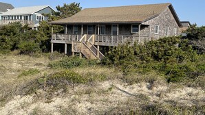 A beachfront house with a wooden deck and stairs leading to a balcony. - Time / Tide 4 Bedroom Cottage by RedAwning (Hatteras)