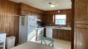 A kitchen with wooden cabinets, a refrigerator, stove, and a dining table with chairs. - Time / Tide 4 Bedroom Cottage by RedAwning (Hatteras)