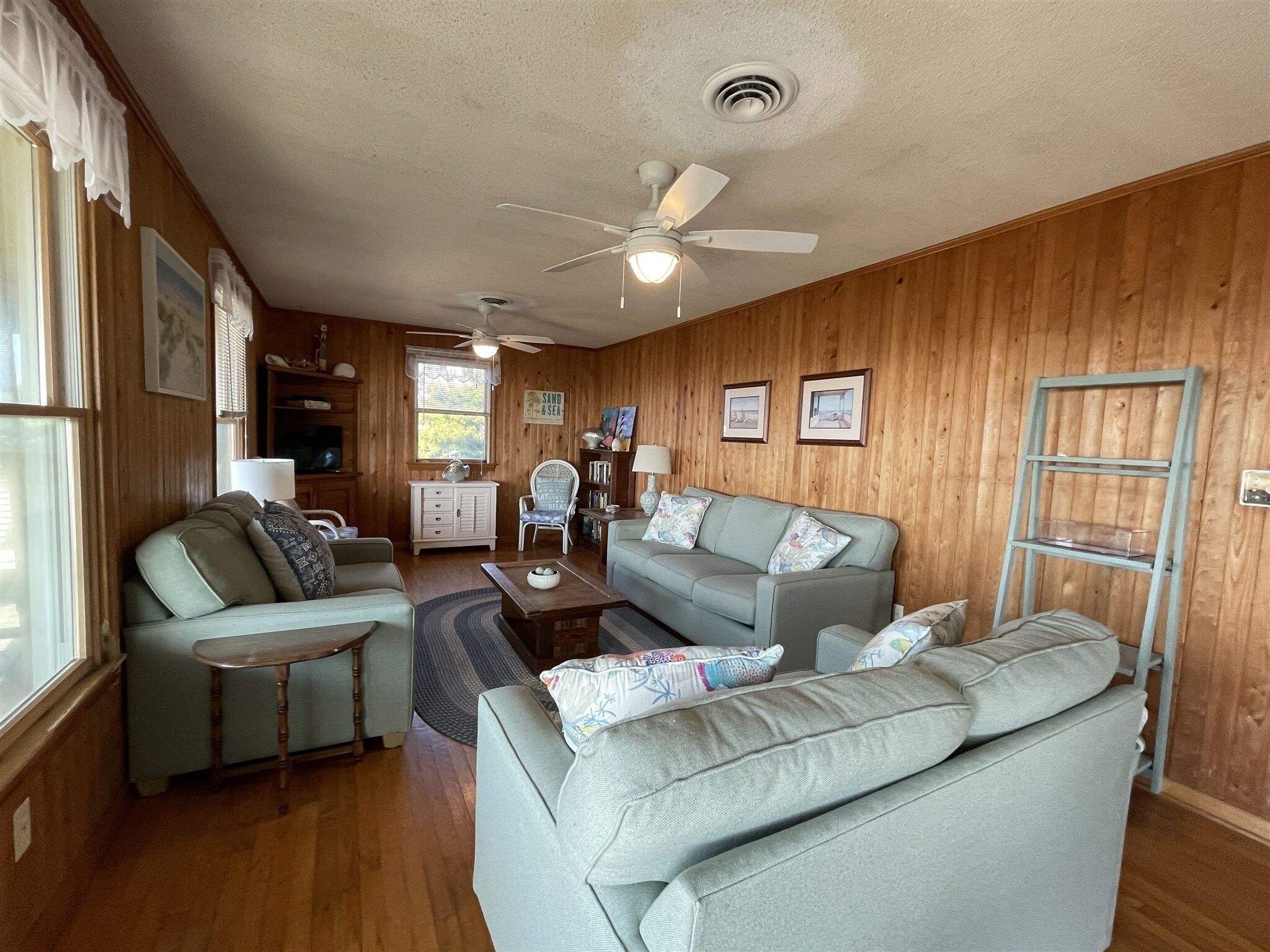 A cozy living room with a wooden wall, a ceiling fan, a sofa, a coffee table, and a side table.