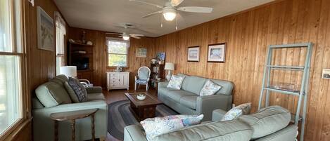 A cozy living room with a wooden wall, a ceiling fan, a sofa, a coffee table, and a side table.