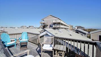 A wooden deck with chairs and a table, overlooking a beach with buildings in the background.