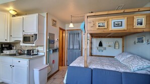 A compact room with a kitchenette, a bed with a bunk, and a small bathroom. - 27 Oceans Door East Studio Bedroom Condo by RedAwning (Hatteras)