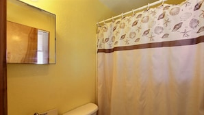 A bathroom with a toilet, sink, and a shower curtain with a sea shell pattern. - 40 Hatteras Blew Studio Bedroom Condo by RedAwning (Hatteras)