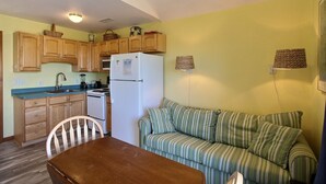 A compact kitchen with wooden cabinets, a refrigerator, a stove, and a dining table with chairs.