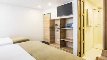 Ein Hotelzimmer mit einem Bett, einem an der Wand befestigten Fernseher, einer Duschkabine und eingebauten Regalen mit Pflanze und Radio.