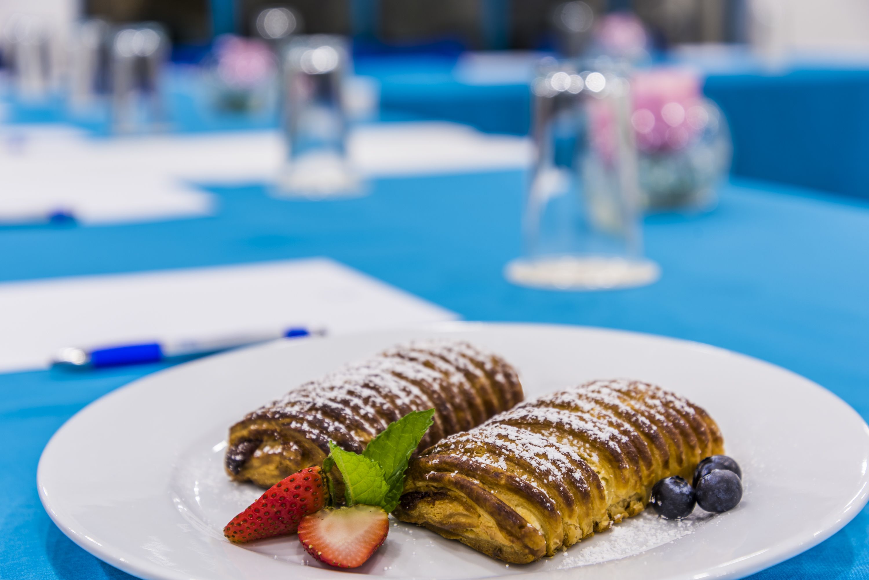A plate of pastries with strawberries and blueberries on a blue tablecloth.