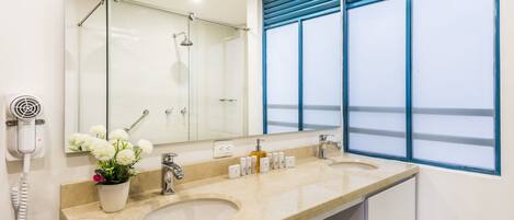 A bathroom with two sinks, a large mirror, a hairdryer, and a window with blue blinds.