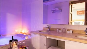 A modern bathroom with a bathtub, two sinks, and a vanity. There are candles, a bucket, and a fruit plate on the vanity.