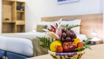 A fruit bowl on a table in a hotel room with a bed and a nightstand in the background.