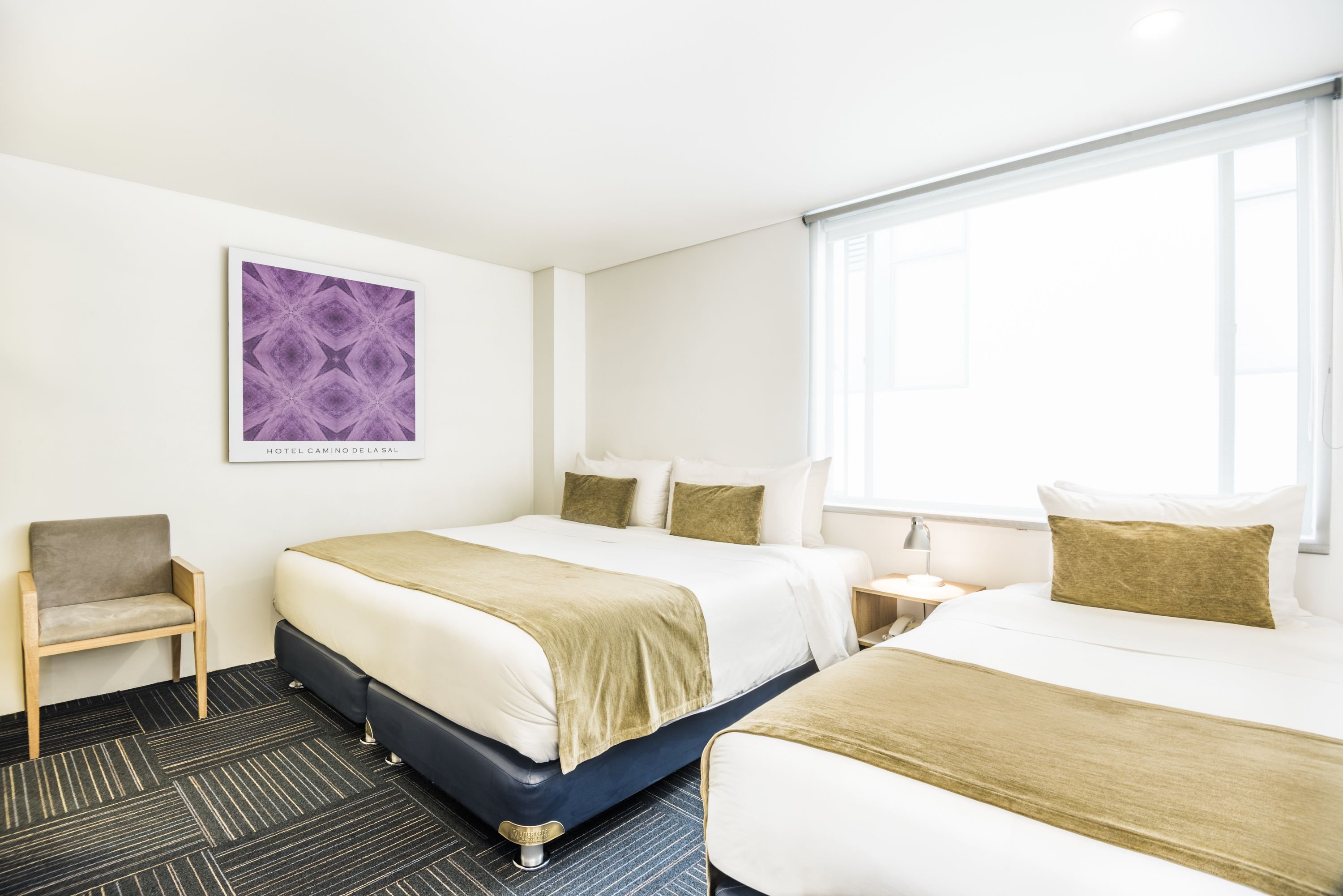 A hotel room with two beds, a chair, a nightstand, and a window.