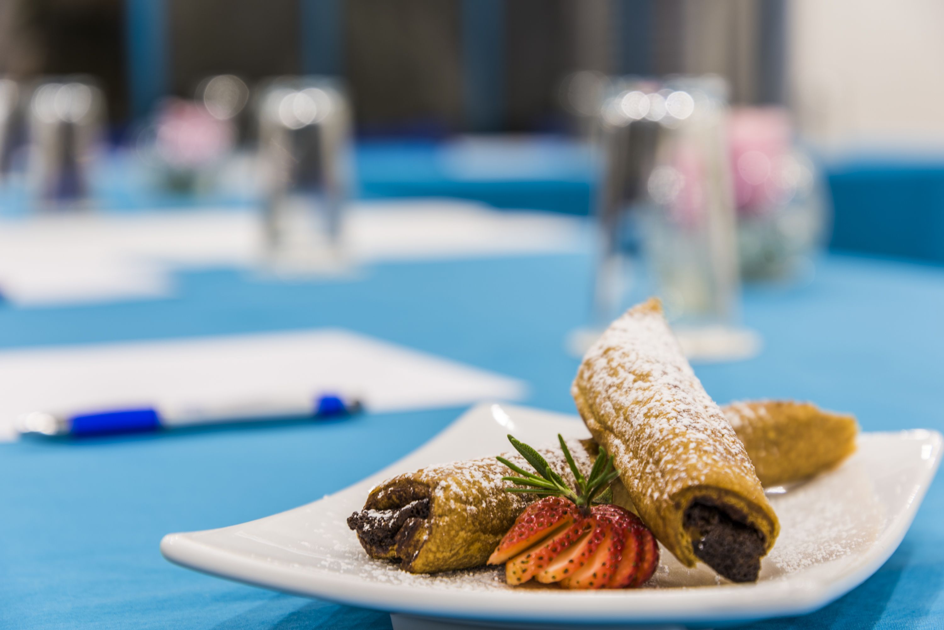 A dessert plate with a rolled pastry and strawberries on a blue tablecloth.