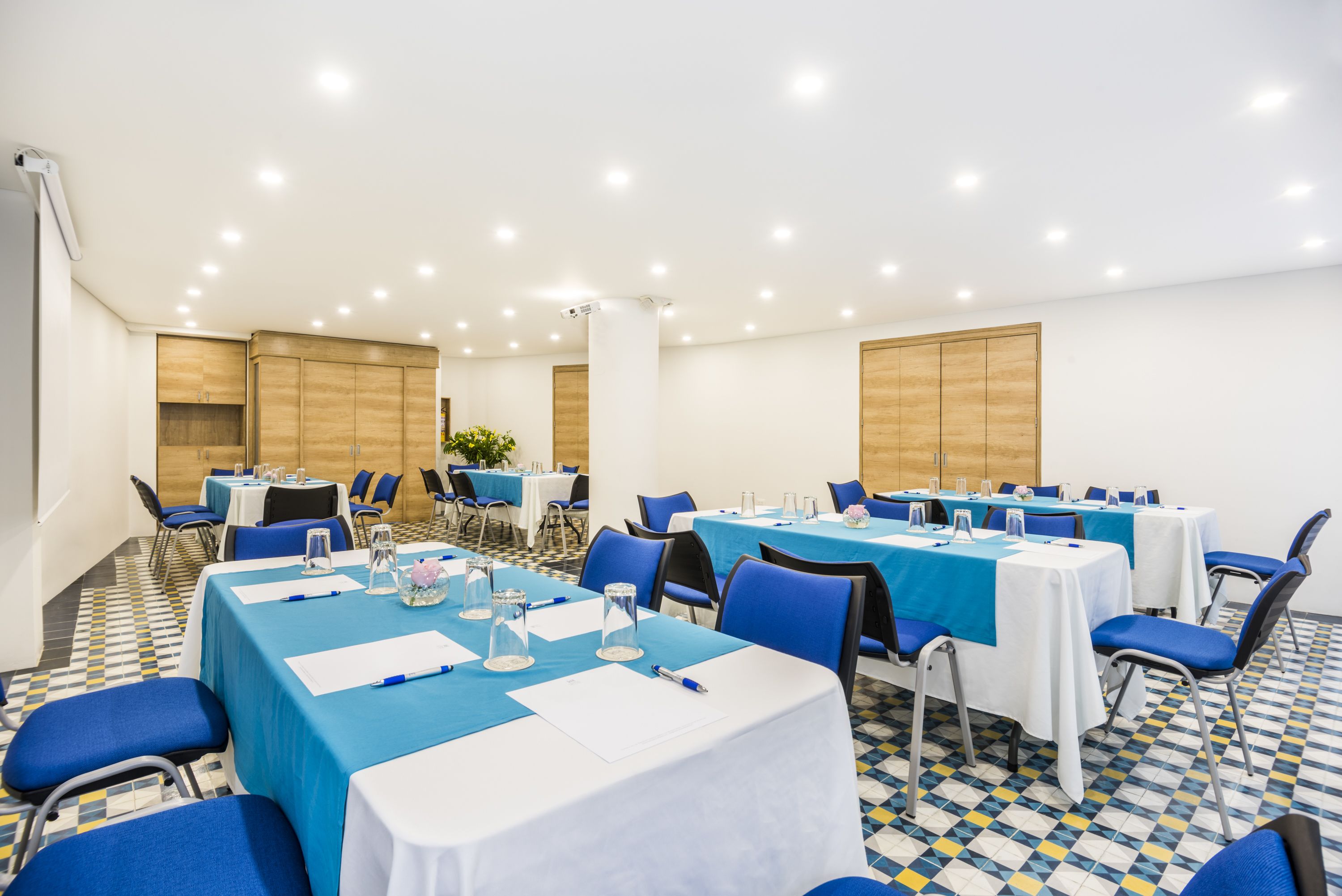 A conference room with tables set for meetings, equipped with chairs and tables, and a tiled floor.