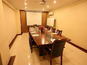 Une salle de conférence équipée d’une longue table, de chaises, d’un projecteur et d’un tableau blanc.