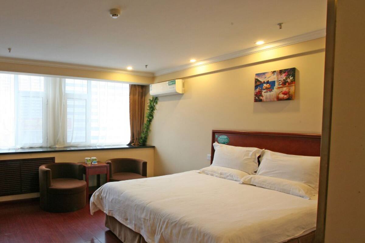 Ein Hotelzimmer mit einem großen Bett, einem kleinen Tisch, zwei Stühlen, einem Fenster mit Vorhängen und einem Bild an der Wand.