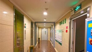 A hotel corridor with a polished floor, a digital exit sign, and a poster on the wall. - Greentree Inn Qinghuangdao Sun City Hotel (Qinhuangdao)