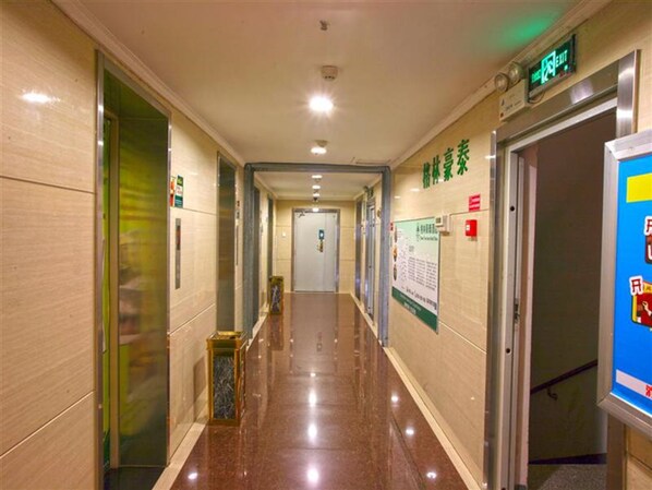 A hotel corridor with a polished floor, a digital exit sign, and a poster on the wall. - Greentree Inn Qinghuangdao Sun City Hotel (Qinhuangdao)
